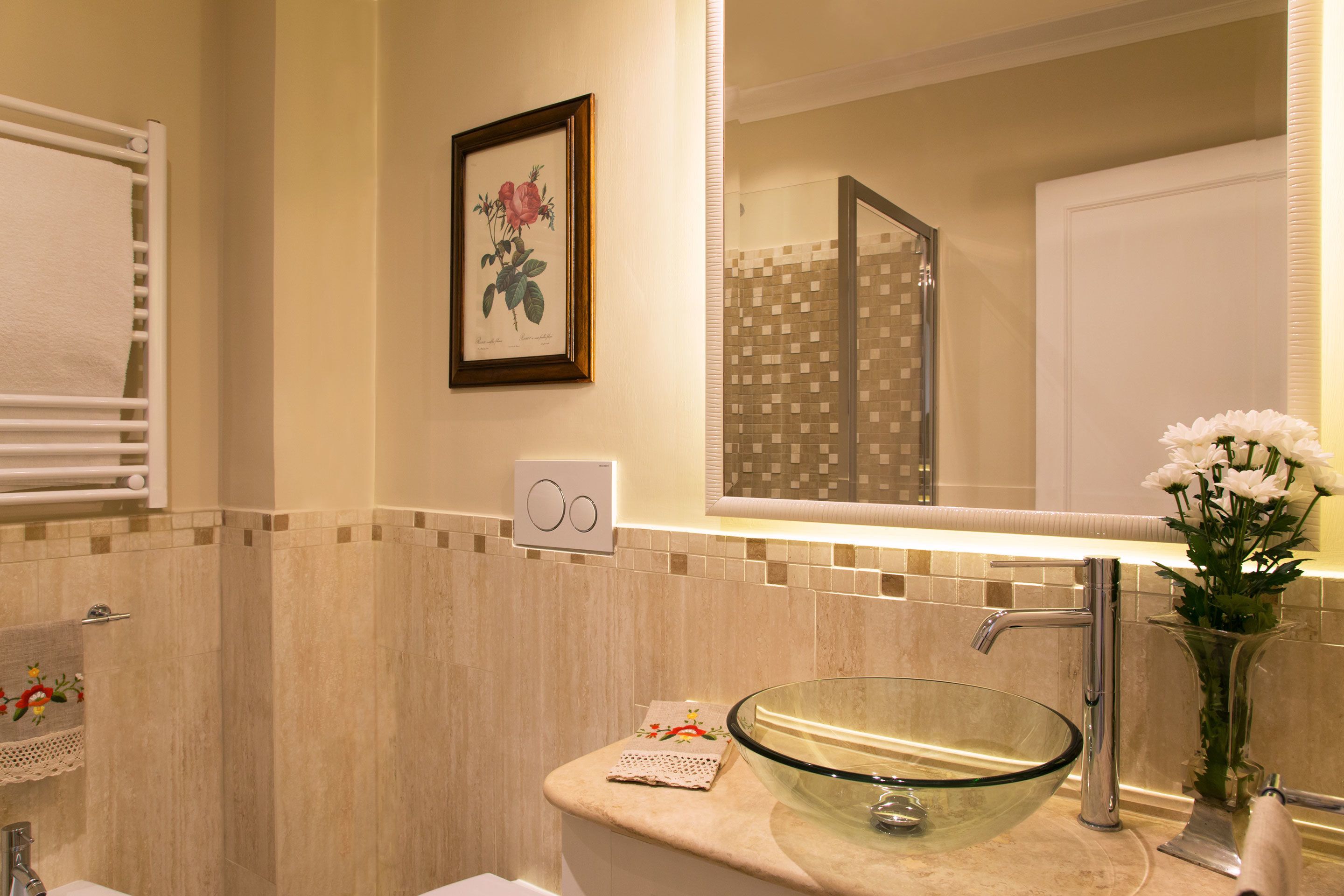 A modern bathroom with a glass bowl sink, a large mirror, a framed botanical print, and a towel rack.