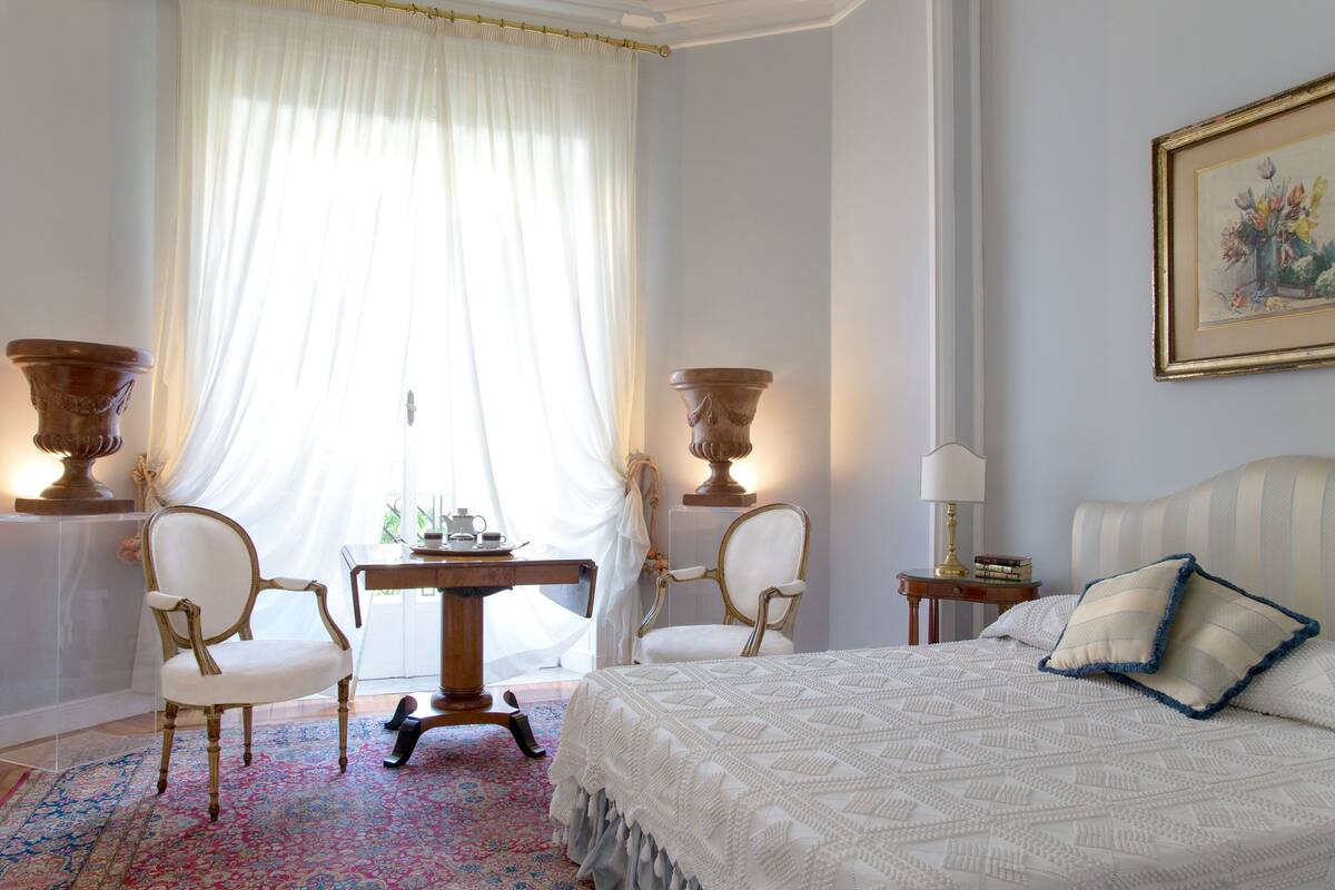 A bedroom with a large bed, two chairs, a table, and two side tables.