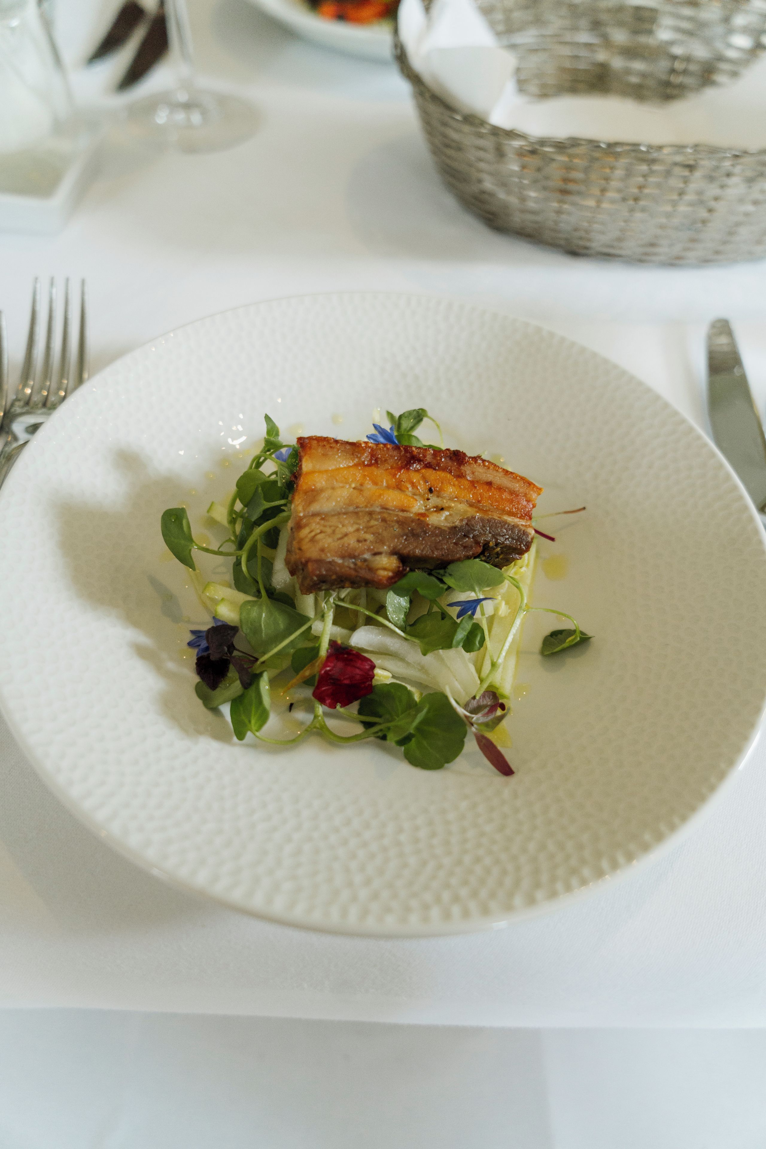 Un plato con un trozo de carne y vegetales sobre un plato blanco con textura.