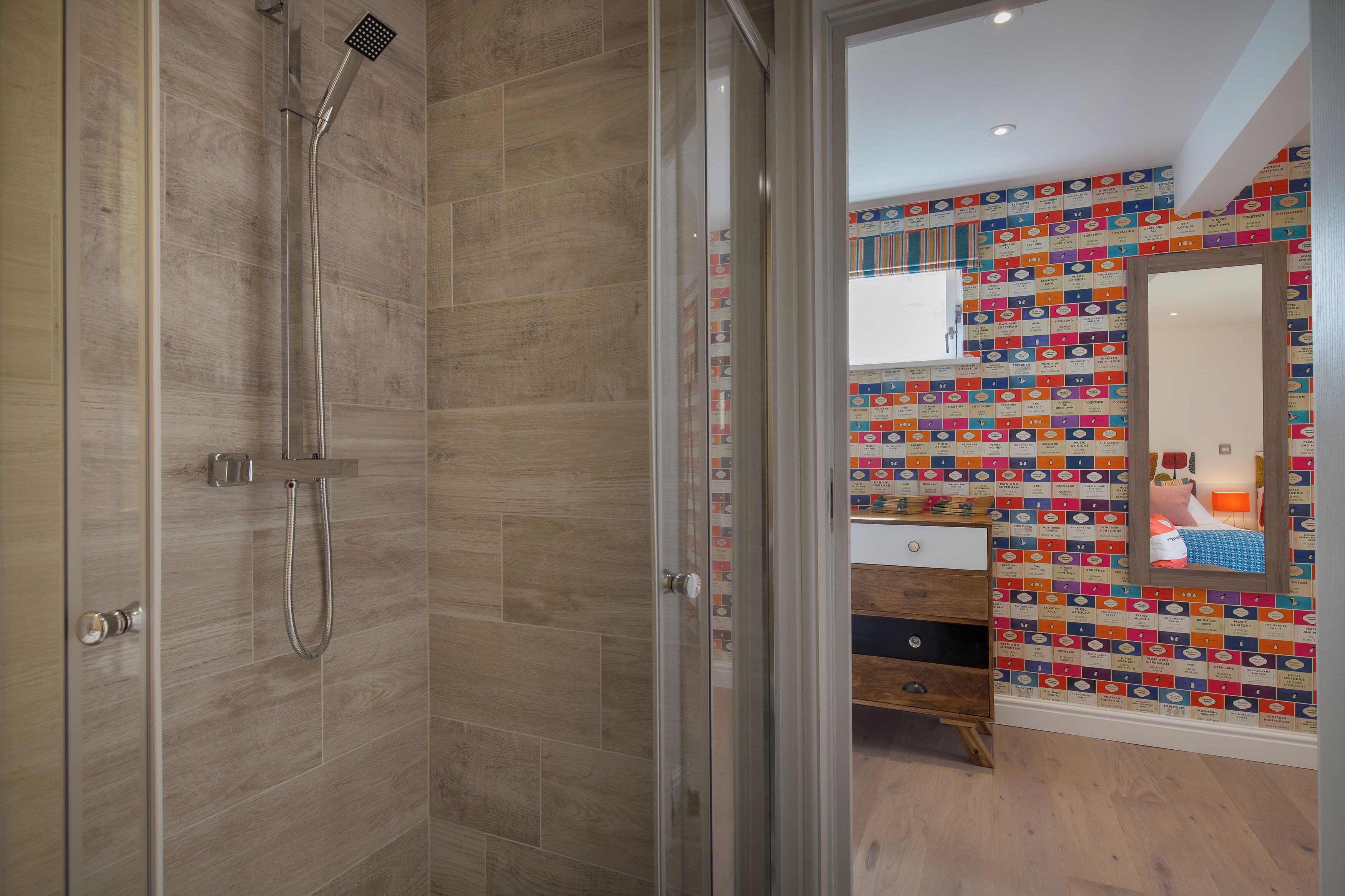 Un baño moderno con ducha, tocador de madera y pared colorida con espejo.