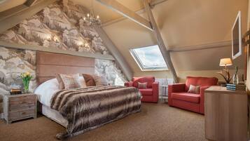 Un dormitorio acogedor con una cama grande, un sillón rojo, una mesita de noche con una lámpara y vistas al cielo a través de un tragaluz.