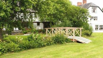 A white house with a wooden bridge and lush greenery.