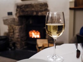 Una copa de vino blanco sobre una mesa, con una chimenea de piedra al fondo.