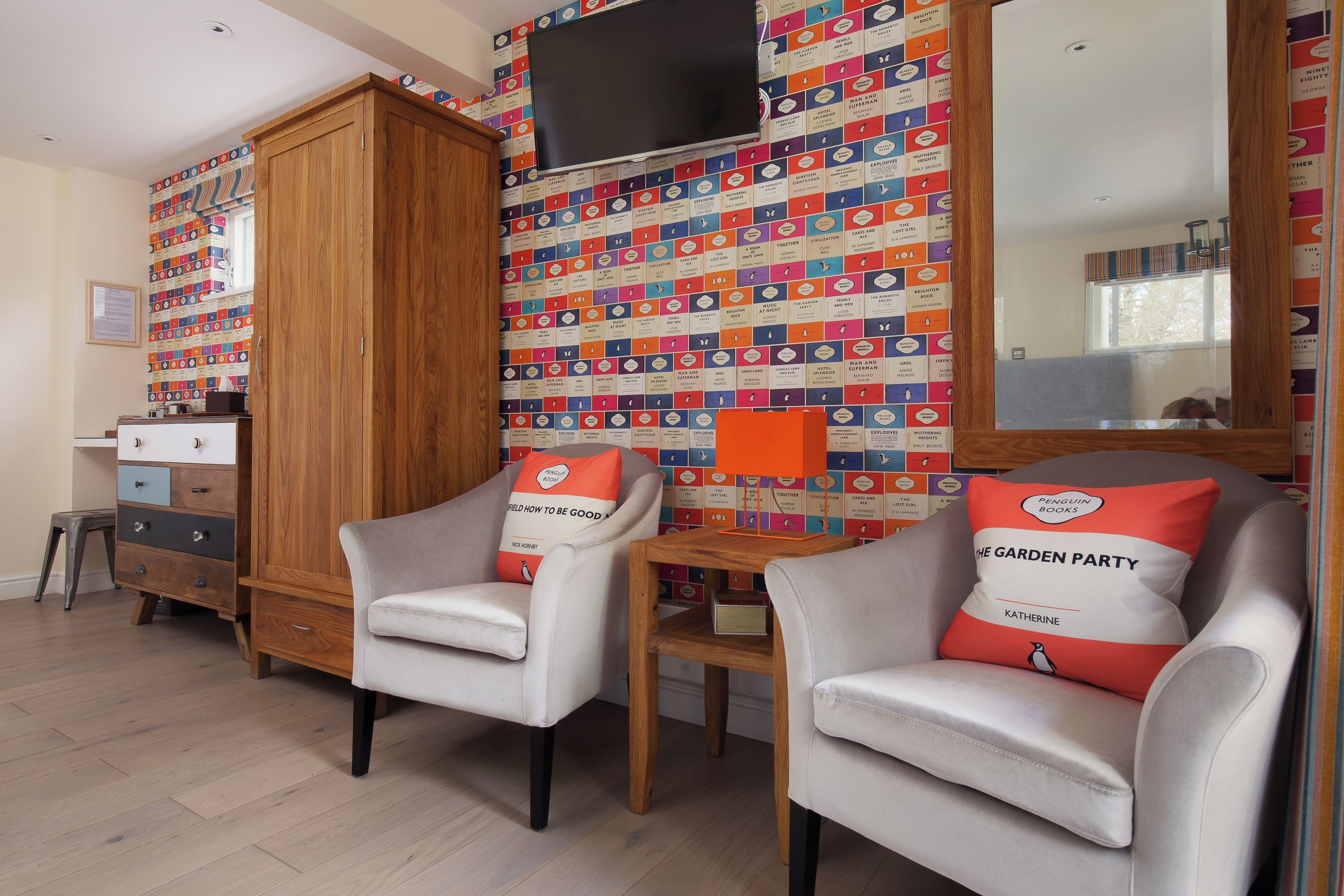 A room with two armchairs, a wooden cabinet, and a wall with colorful book covers.