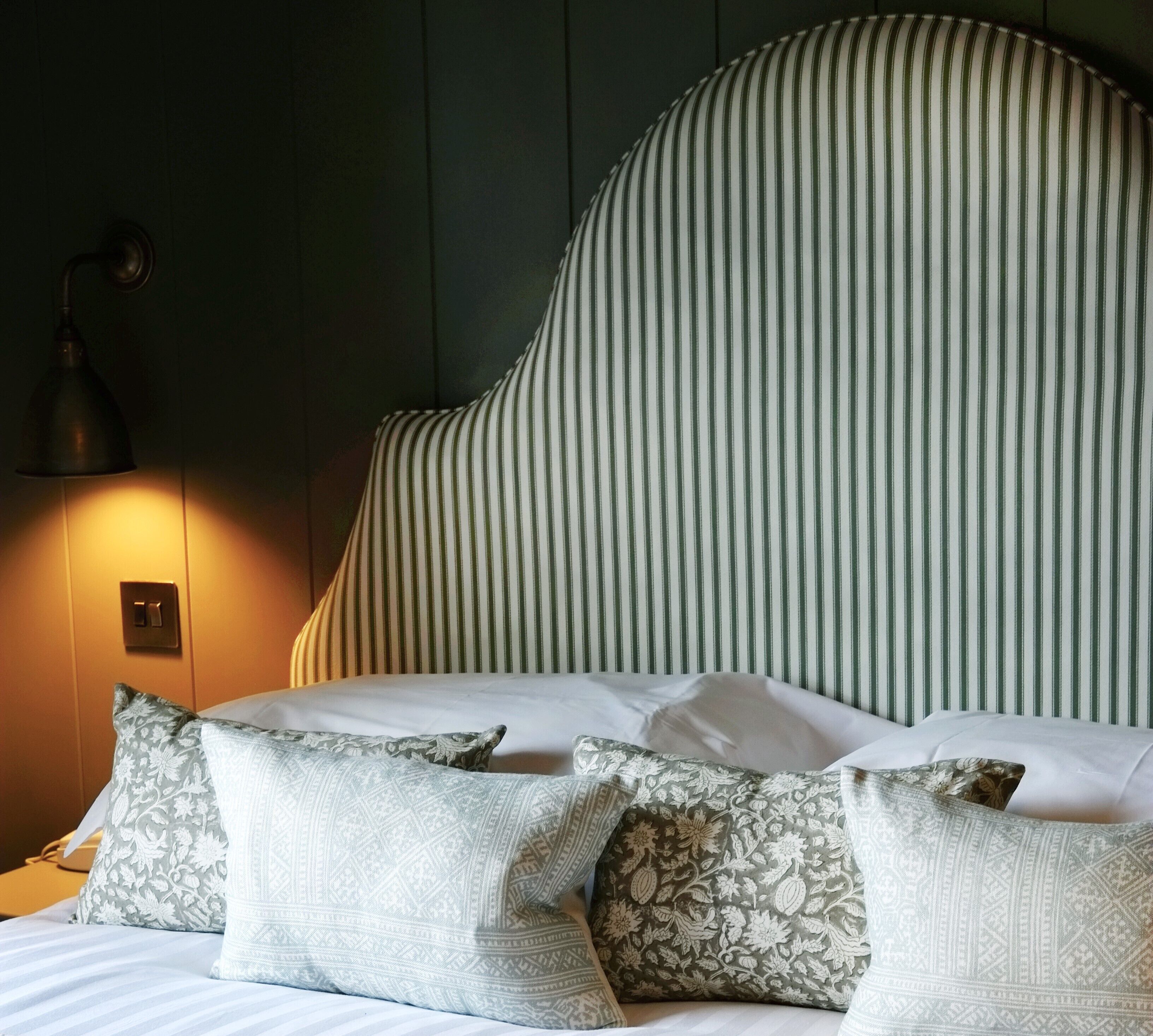 A bed with striped headboard, patterned pillows, and a wall-mounted lamp.