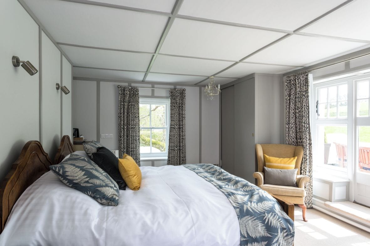 A bedroom with a large bed, a chair, a window, and a view of the outdoors.