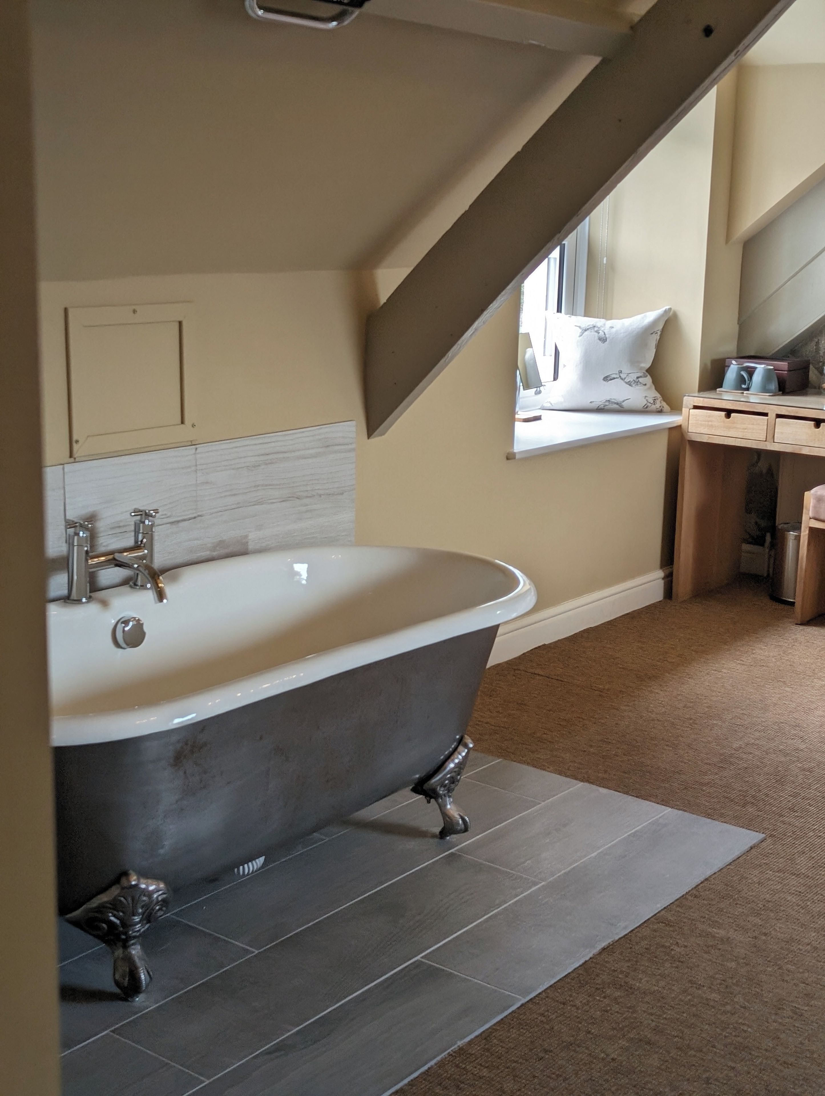 Une salle de bain avec une baignoire sur pieds, une fenêtre offrant une belle vue et un meuble-lavabo en bois doté de tiroirs.