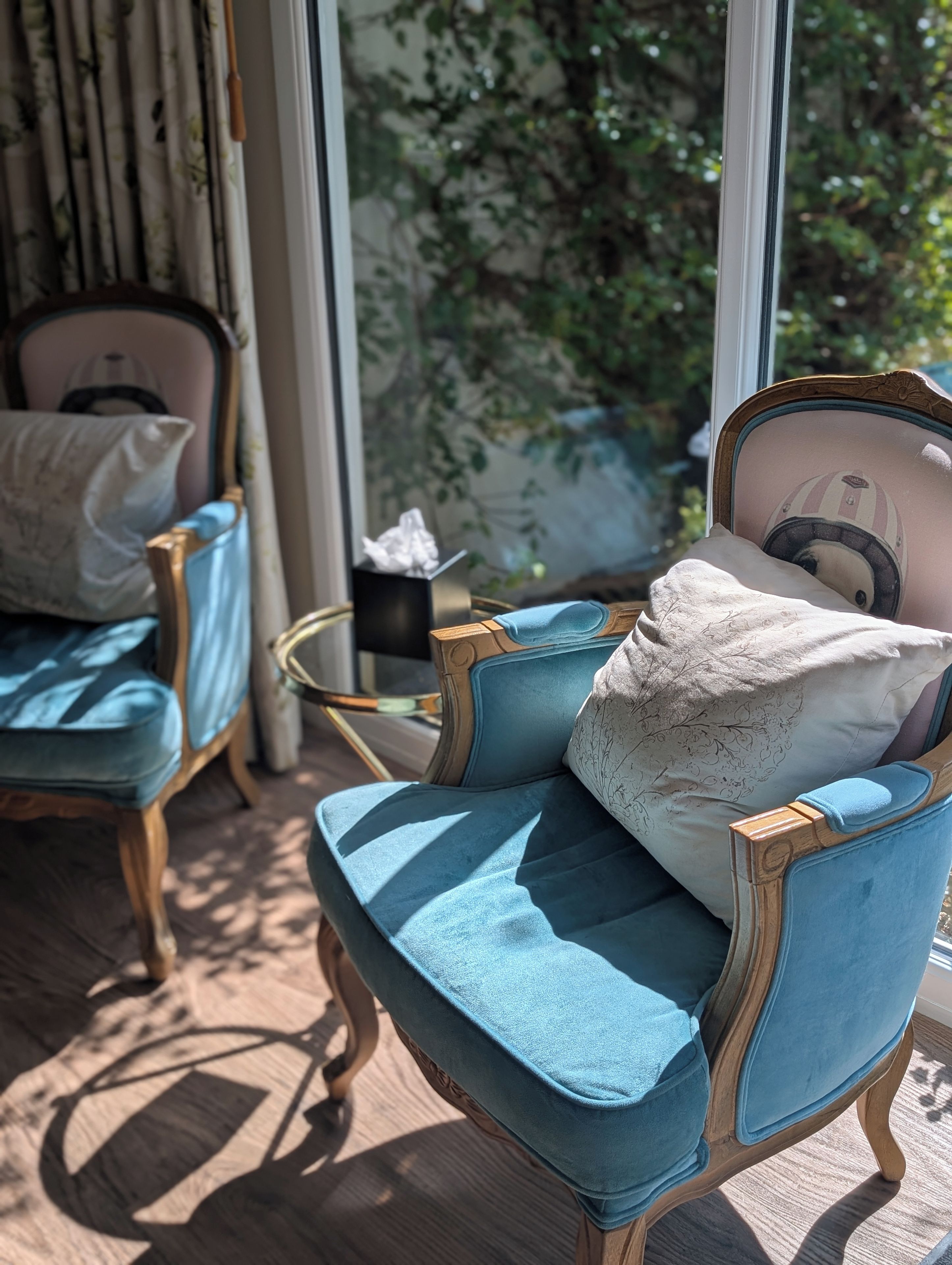 Une pièce comprenant un fauteuil bleu recouvert de tissu, un pouf assorti et un coussin décoratif. On y trouve également une petite table ronde sur laquelle est posée une boîte de mouchoirs.