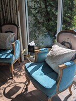 A room with a blue upholstered chair, a matching ottoman, and a decorative pillow. There is a small round table with a tissue box on it.
