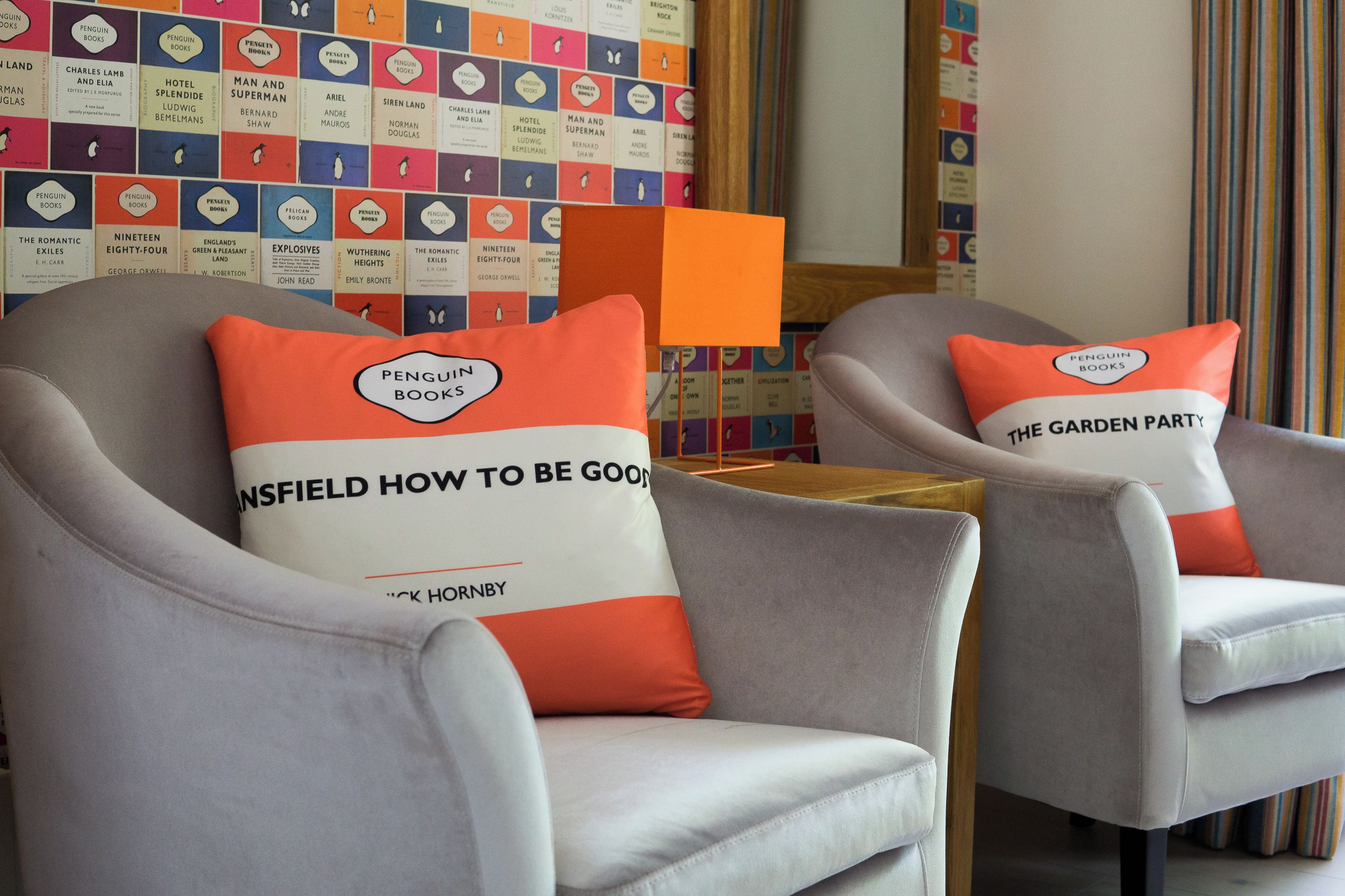 Two armchairs with matching cushions, a small orange table, and a wall with colorful book spines.