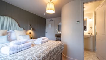 Una cama bien hecha con toallas dobladas, una lámpara de noche y un espejo adosado a la pared en una habitación de hotel.