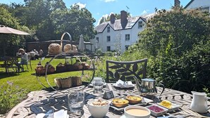 An outdoor dining table set with various dishes, glasses, and utensils, surrounded by a garden and a building in the background. - Mill End Hotel (Newton Abbot)