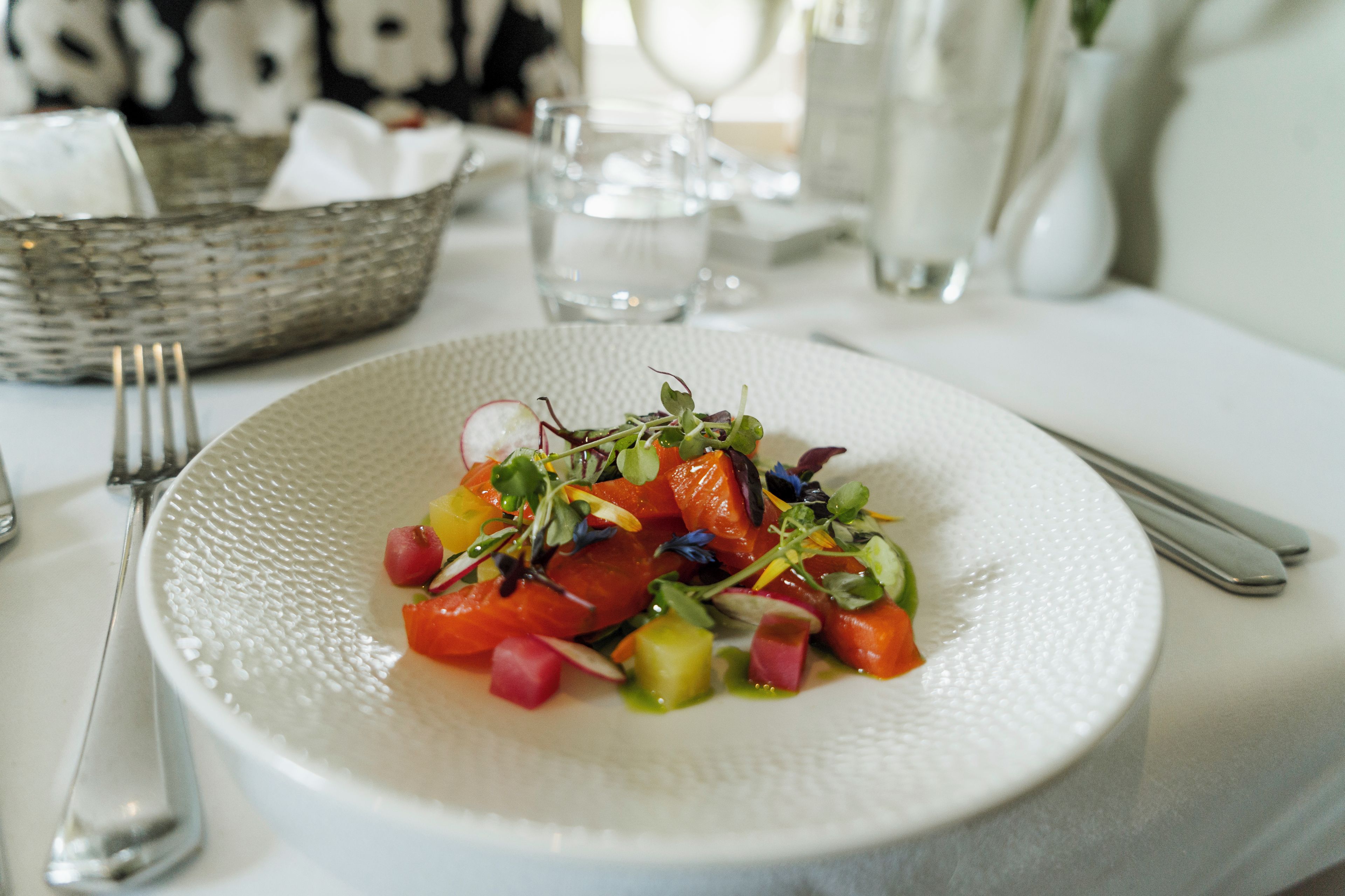 A white textured plate with a colorful salad, a fork, and a knife on a table.
