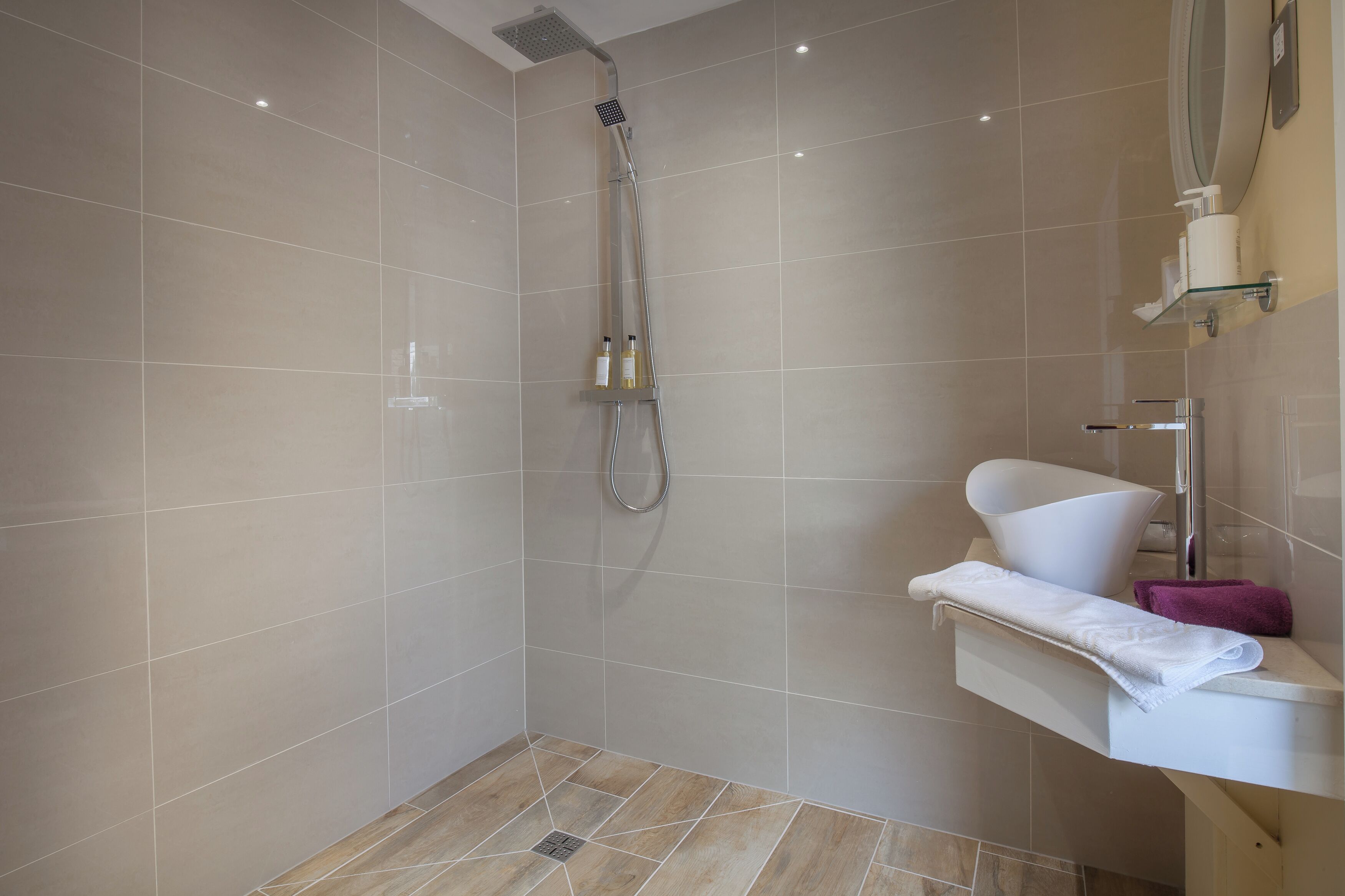 A modern bathroom with a shower, a white sink, and a glass shelf with toiletries.