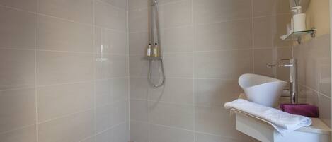 A modern bathroom with a shower, a white sink, and a glass shelf with toiletries.