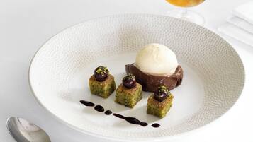 Une assiette de dessert avec une boule de glace, un dessert au chocolat et quatre petits carrés recouverts d’une cerise et de pistaches.