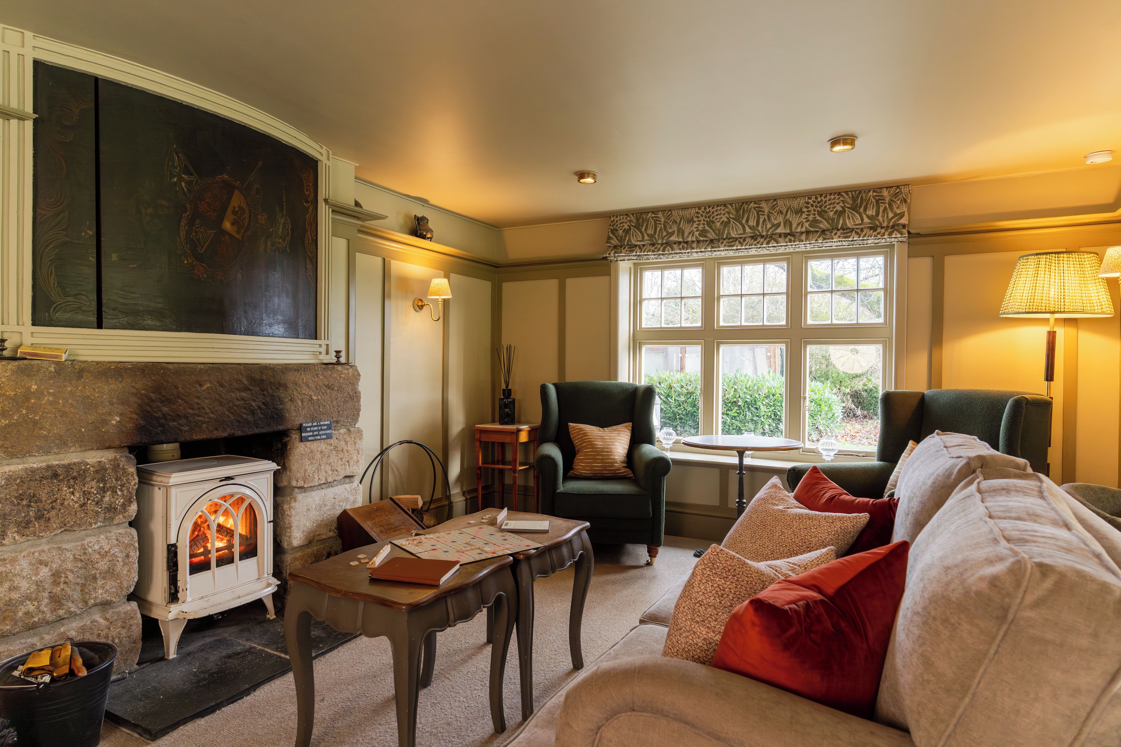 A cozy living room with a fireplace, comfortable seating, and a view of greenery outside.