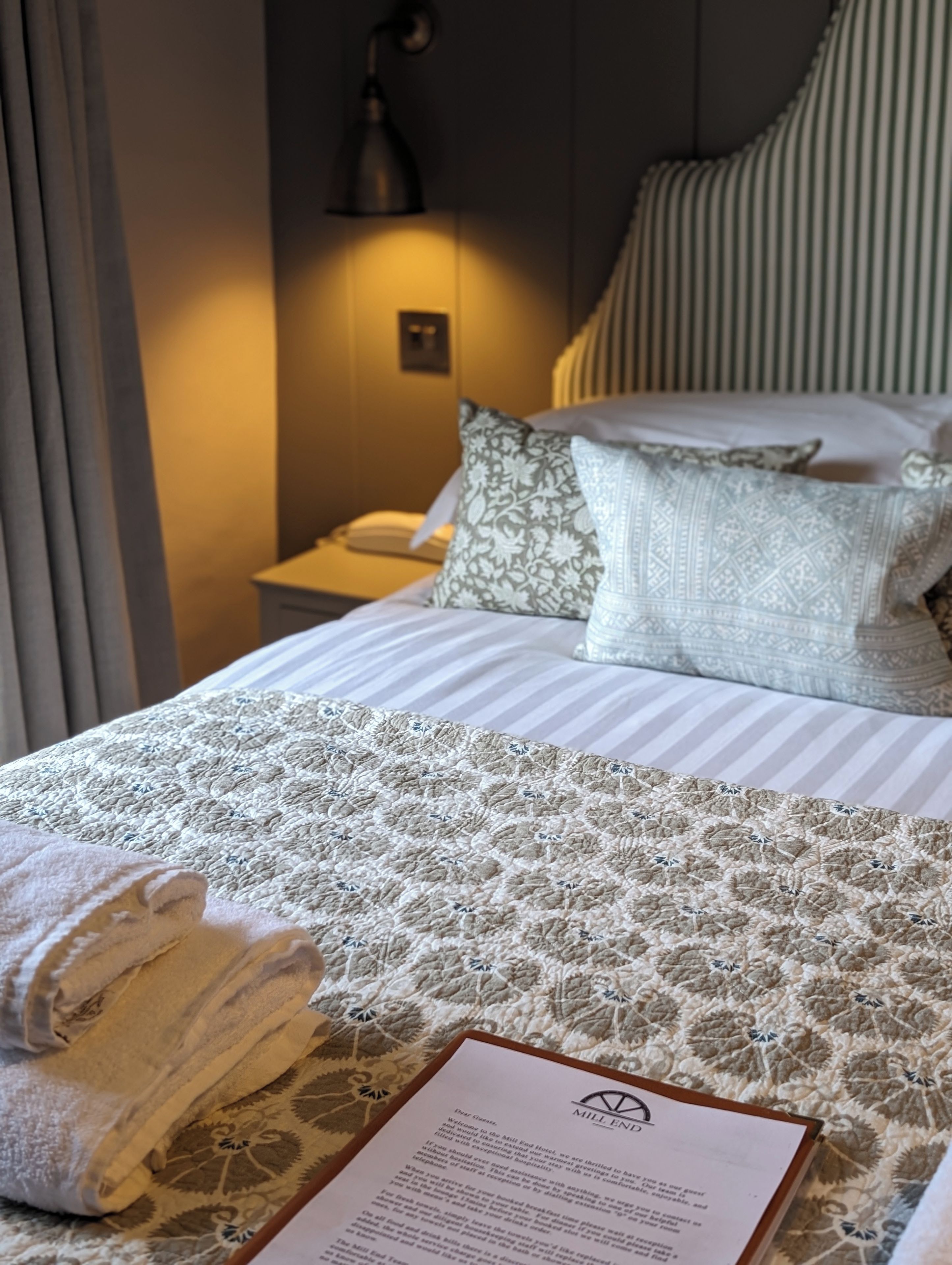 A hotel room with a neatly made bed, a bedside lamp, and a welcome message on the bed.