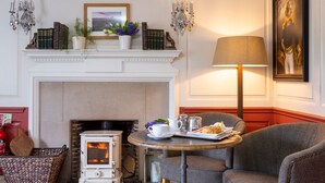 A cozy room with a fireplace, a table with a tray of food, and a comfortable chair. - Mill End Hotel (Newton Abbot)