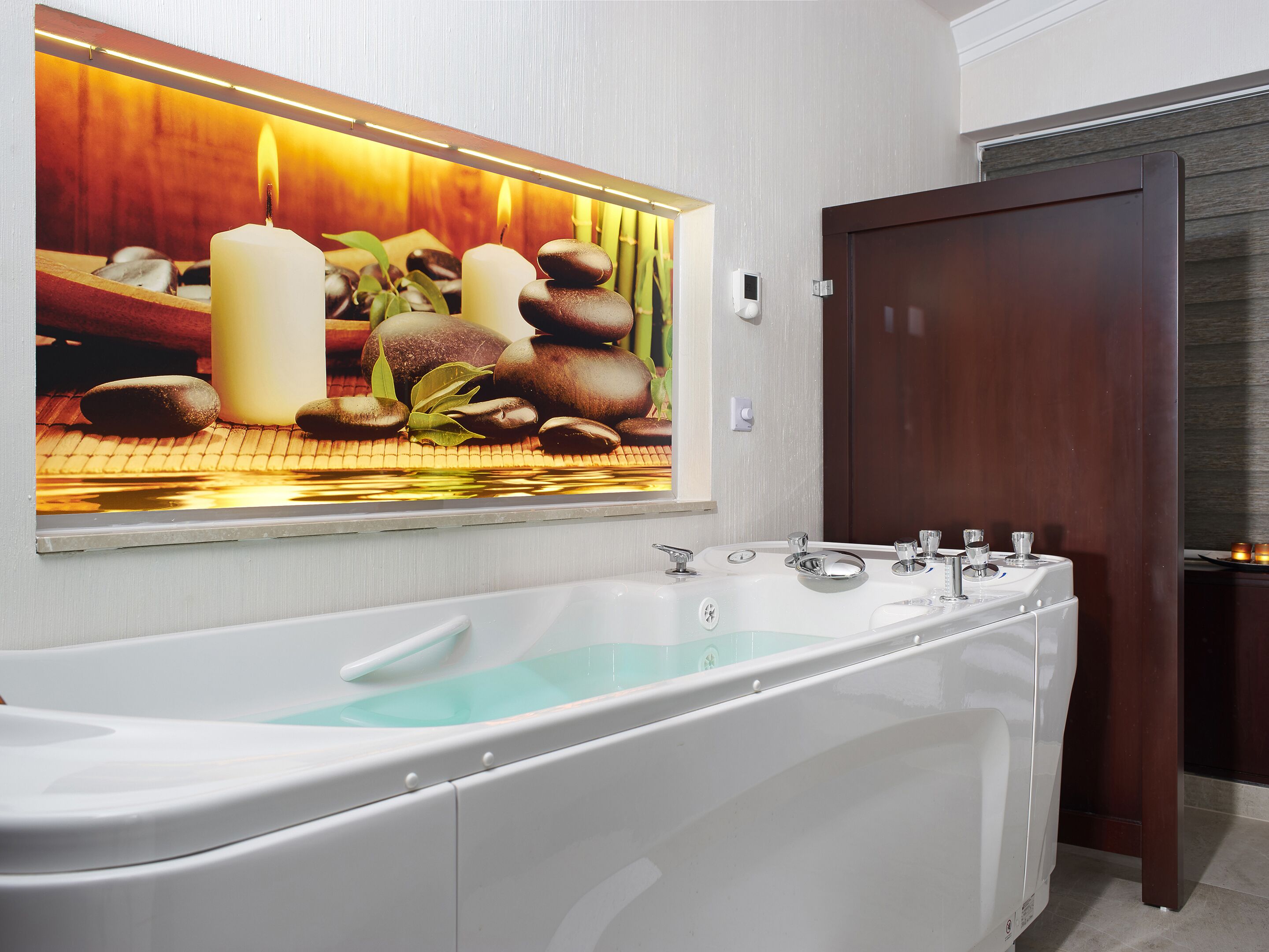 Un baño moderno con una bañera grande, una puerta de madera y un espejo empotrado que refleja un ambiente tipo spa.