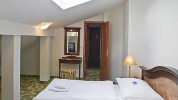 A hotel room with two beds, a desk, a mirror, a lamp, and a skylight.