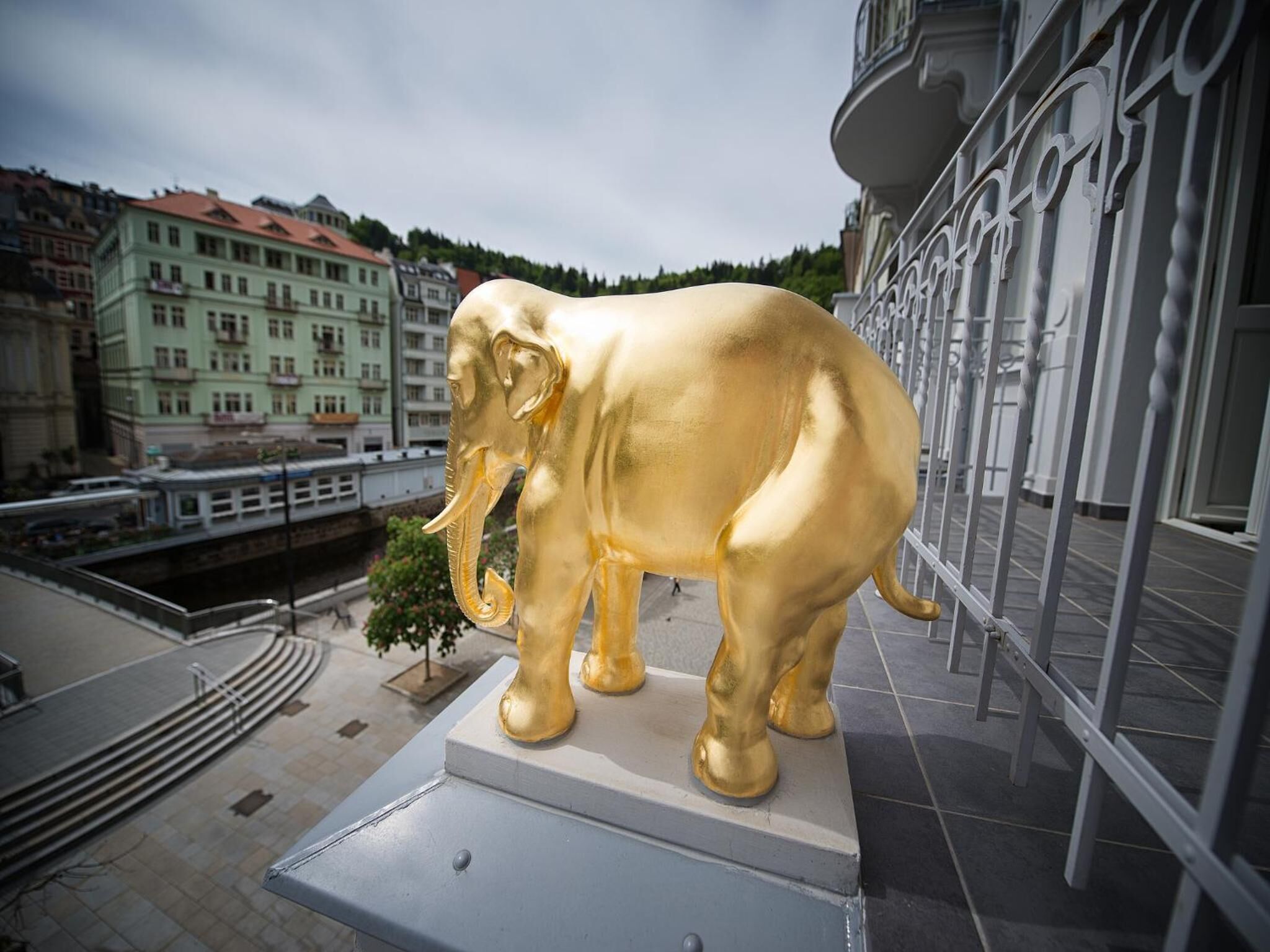 Une statue d’éléphant doré, posée sur un piédestal, dans un environnement urbain, avec des bâtiments et un pont en arrière-plan.