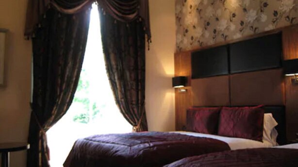 A bedroom with a large bed, dark curtains, a floral wallpaper headboard, and a nightstand.