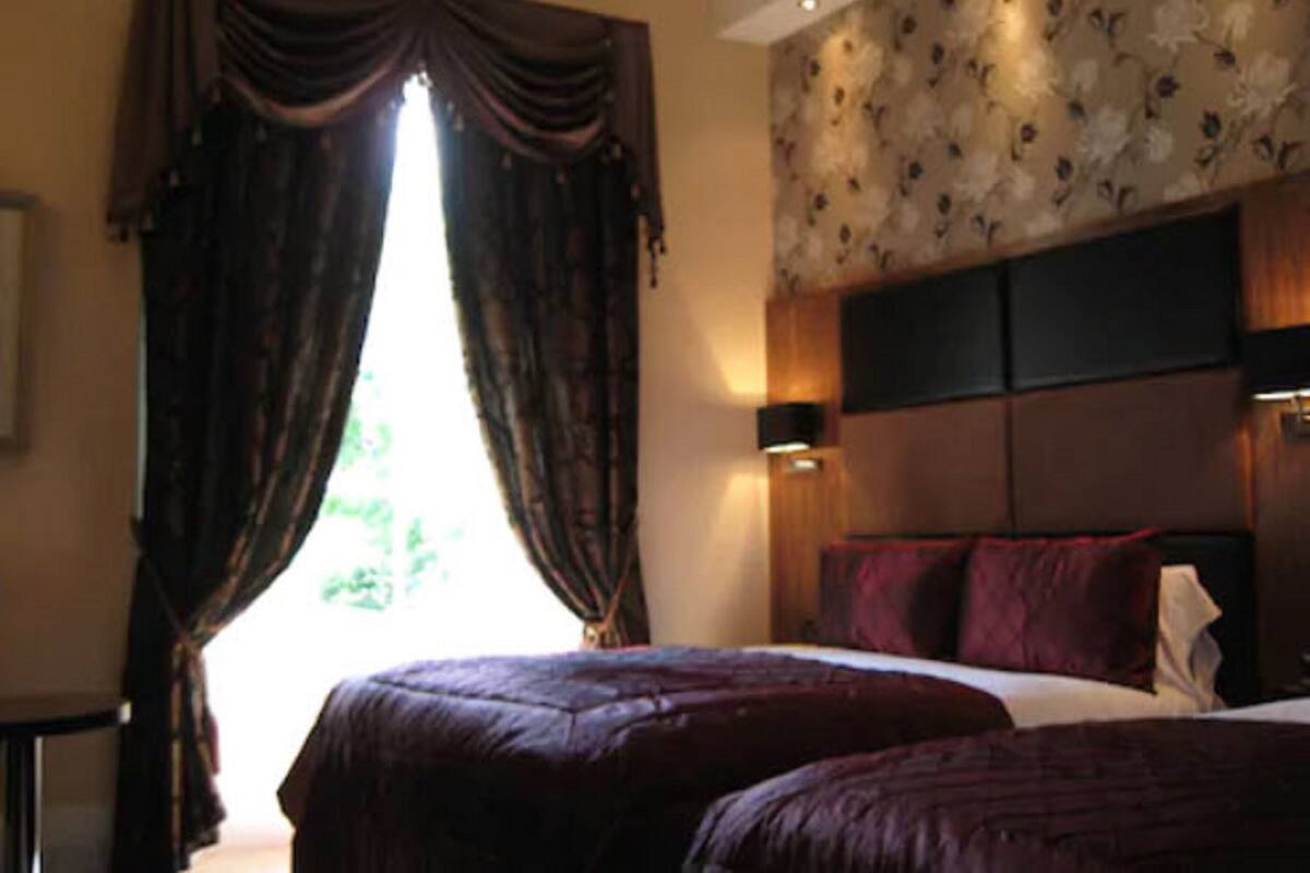 A bedroom with a large bed, dark curtains, a floral wallpaper headboard, and a nightstand.
