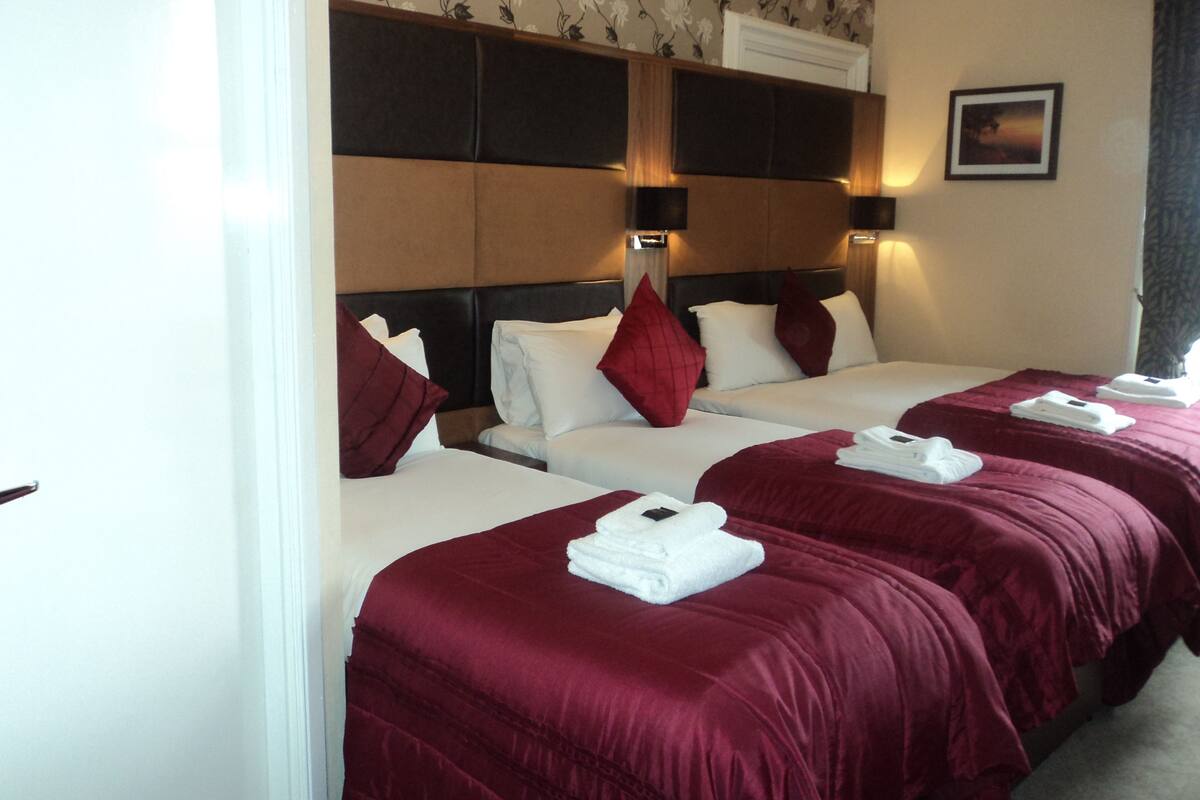 A hotel room with two beds, each with a red bedspread and white pillows. There are wall-mounted light fixtures and a framed picture on the wall.