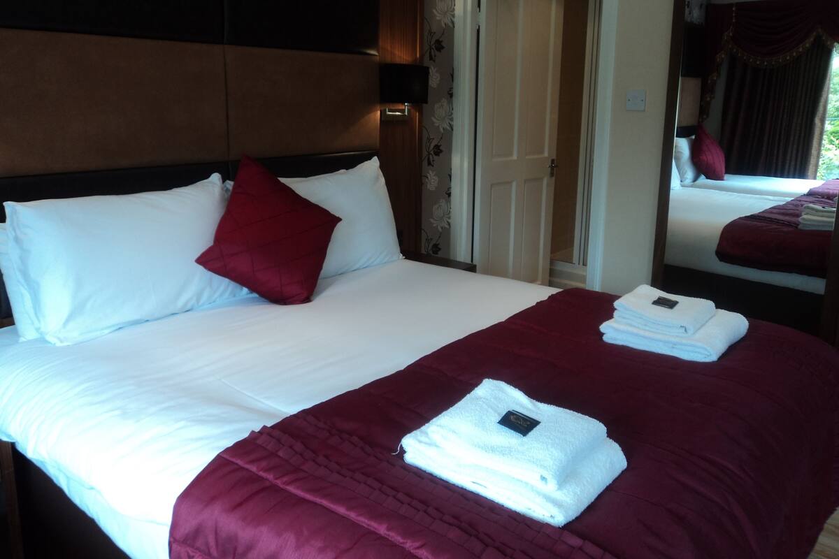 A hotel room with a large bed, a headboard, a mirror, and a door leading to another room.