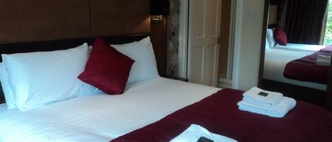 A hotel room with a large bed, a headboard, a mirror, and a door leading to another room.