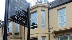 A sign for a guest house with a contact number and a website URL.