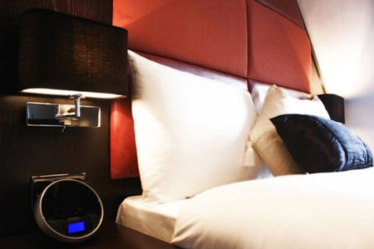 A hotel room with a bed, a nightstand with a lamp, and a digital clock.