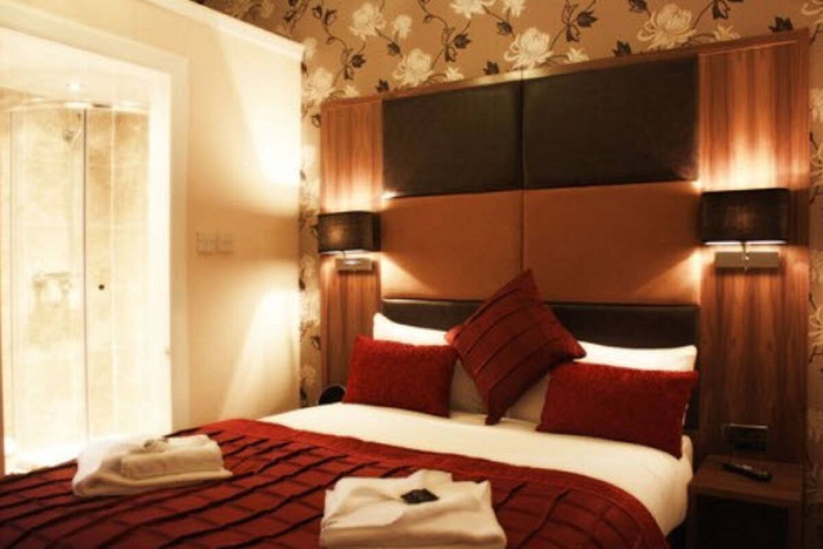 A hotel room with a bed, a nightstand, a lamp, and a window with curtains.