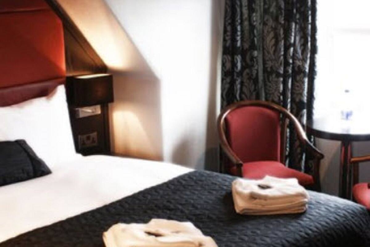 A hotel room with a bed, a red chair, a small table, and a window with curtains.