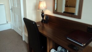 A hotel room with a wooden desk, a lamp, a mirror, and a chair.