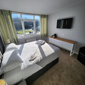 A bedroom with a bed, a TV mounted on the wall, a desk, and a window with curtains. - Kings Knoll Hotel (Oban)