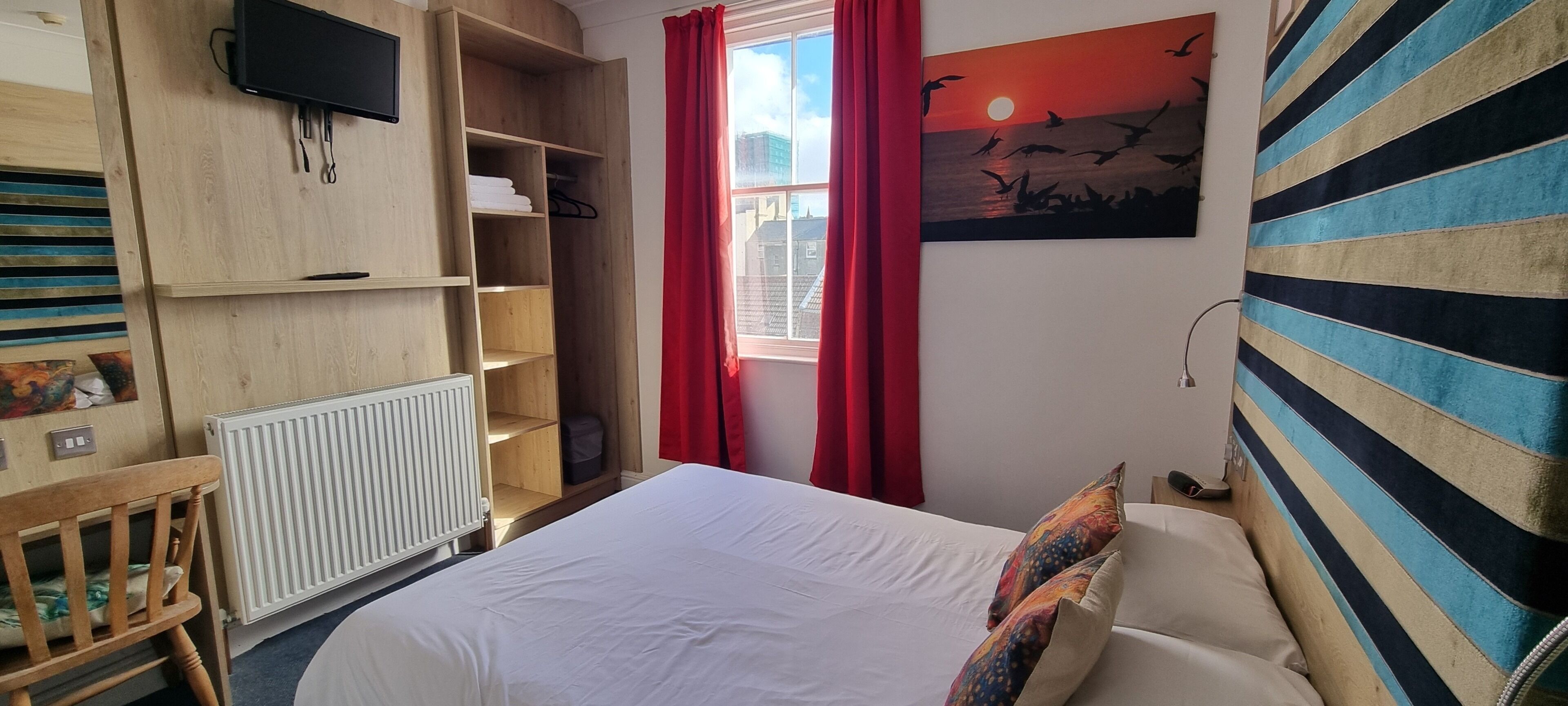 A bedroom with a bed, a wooden wardrobe, a radiator, a TV, and a painting of birds.