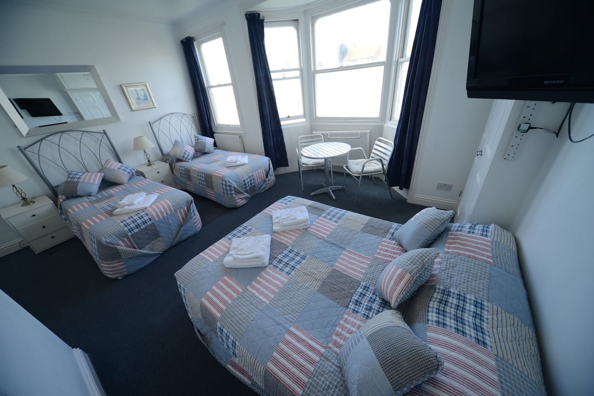A hotel room with two beds, a small table, a chair, a TV, and a window with curtains.