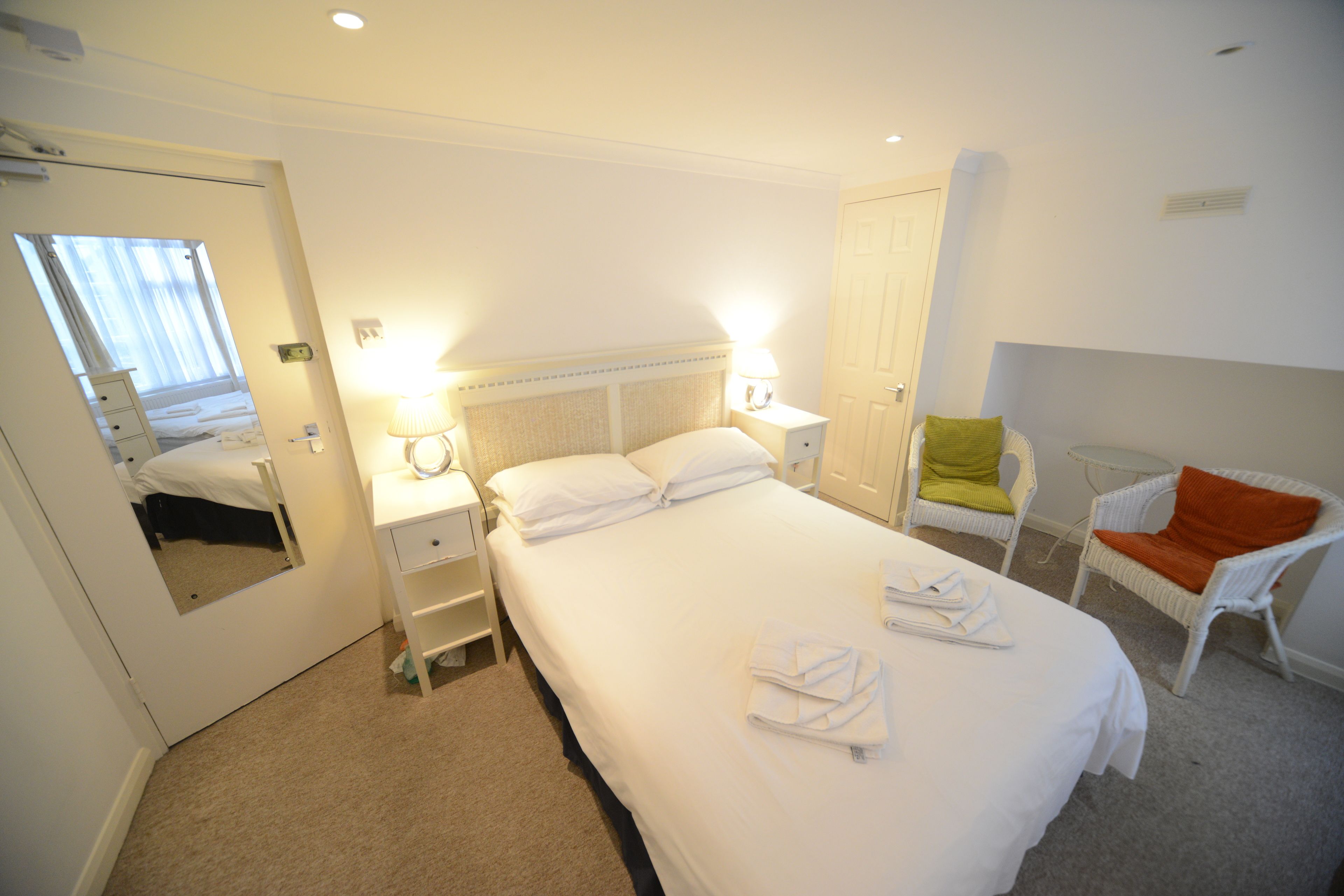 Une chambre d’hôtel avec un grand lit, des tables de chevet avec des lampes, une chaise et un miroir.