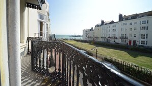 A balcony with ornate black railings overlooking a coastal promenade with white buildings and a clear view of the sea. - Marine View (Brighton)