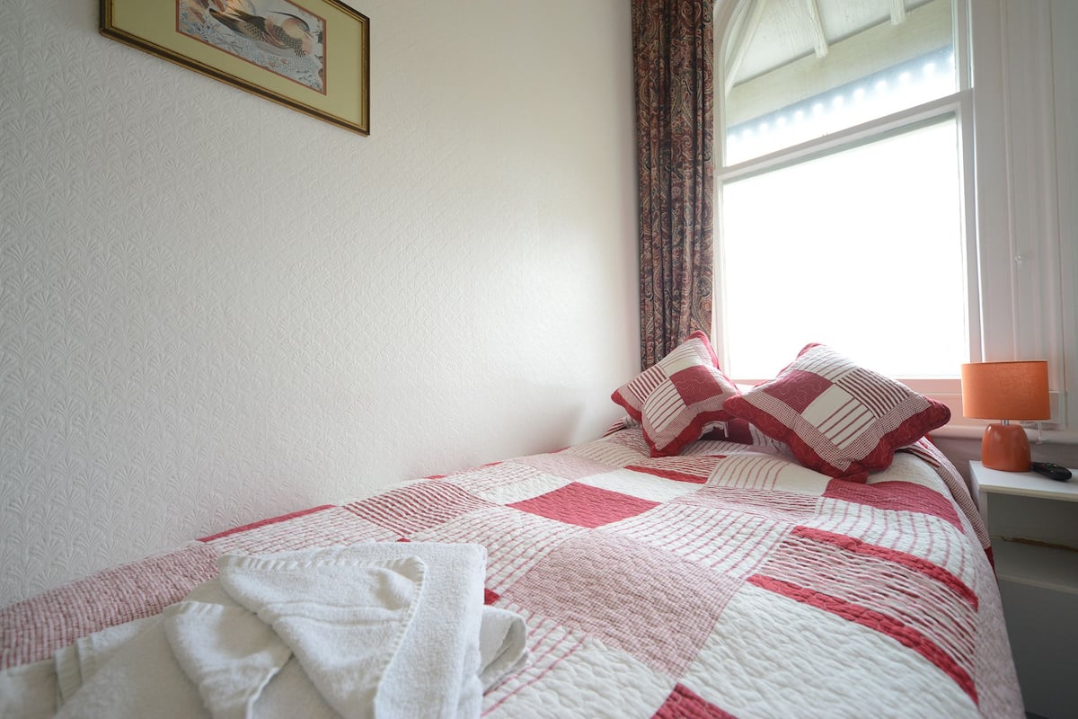 A neatly made bed with a checkered bedspread, a pillow, and a folded towel on the bed.