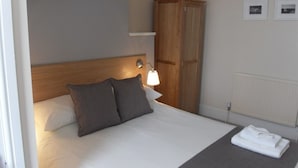A neatly made bed with pillows, a wooden headboard, a bedside lamp, a wardrobe, and a radiator. - Powys Lodge (Scarborough)