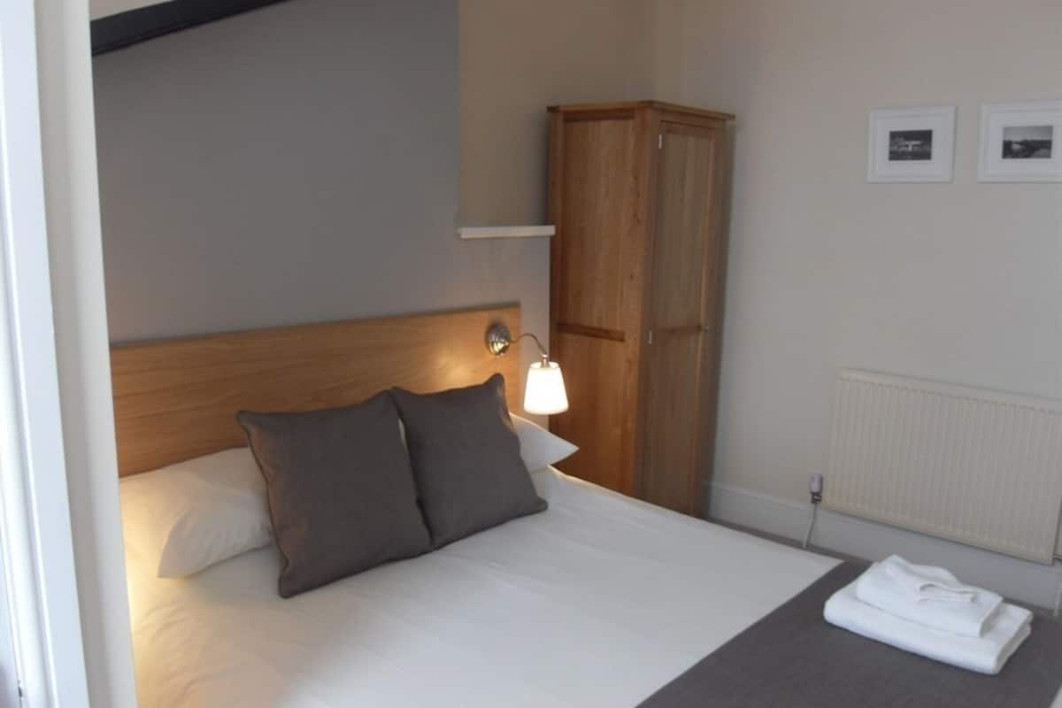 A neatly made bed with pillows, a wooden headboard, a bedside lamp, a wardrobe, and a radiator.
