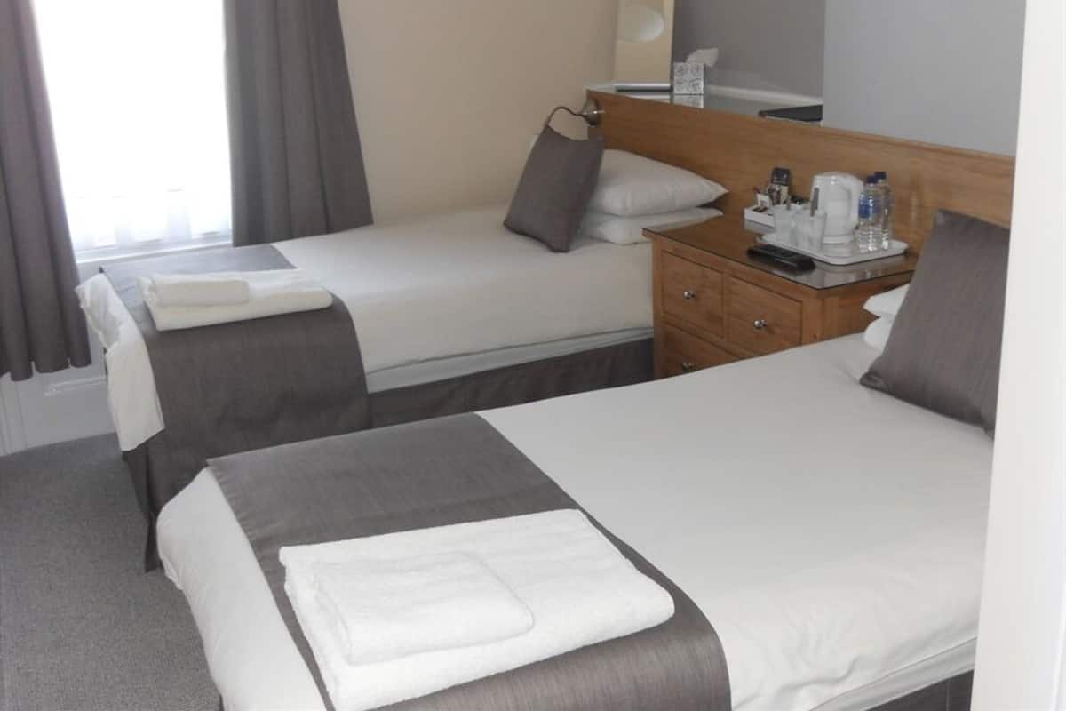 A hotel room with two single beds, a wooden nightstand, a mirror, and a window with curtains.