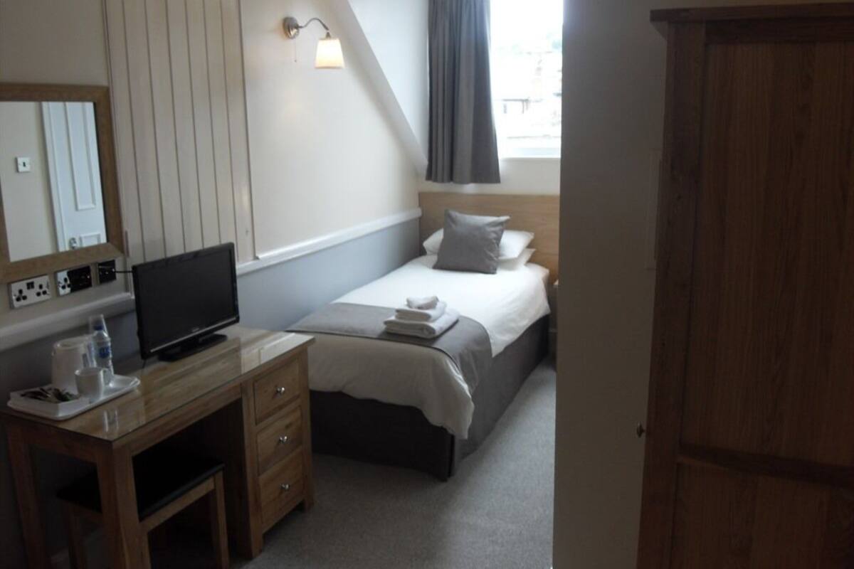 A bedroom with a bed, a desk with a television, a mirror, and a window with curtains.