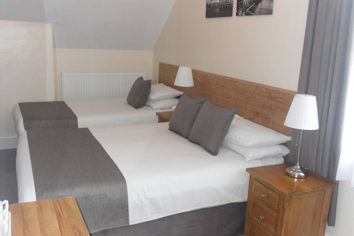 A hotel room with two beds, a wooden nightstand, a lamp, and a radiator.