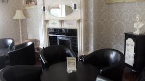 A room with a fireplace, black leather chairs, a small table with a menu, and a bust on a cabinet. - Powys Lodge (Scarborough)