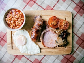 A breakfast plate with sausages, bacon, a fried egg, mushrooms, tomatoes, and baked beans.