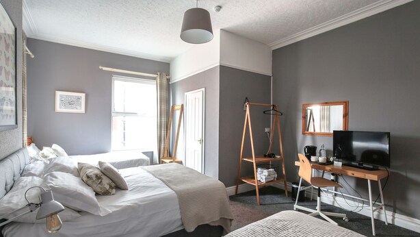Un dormitorio con cama, mesita de noche, lámpara y escritorio con silla y televisor.